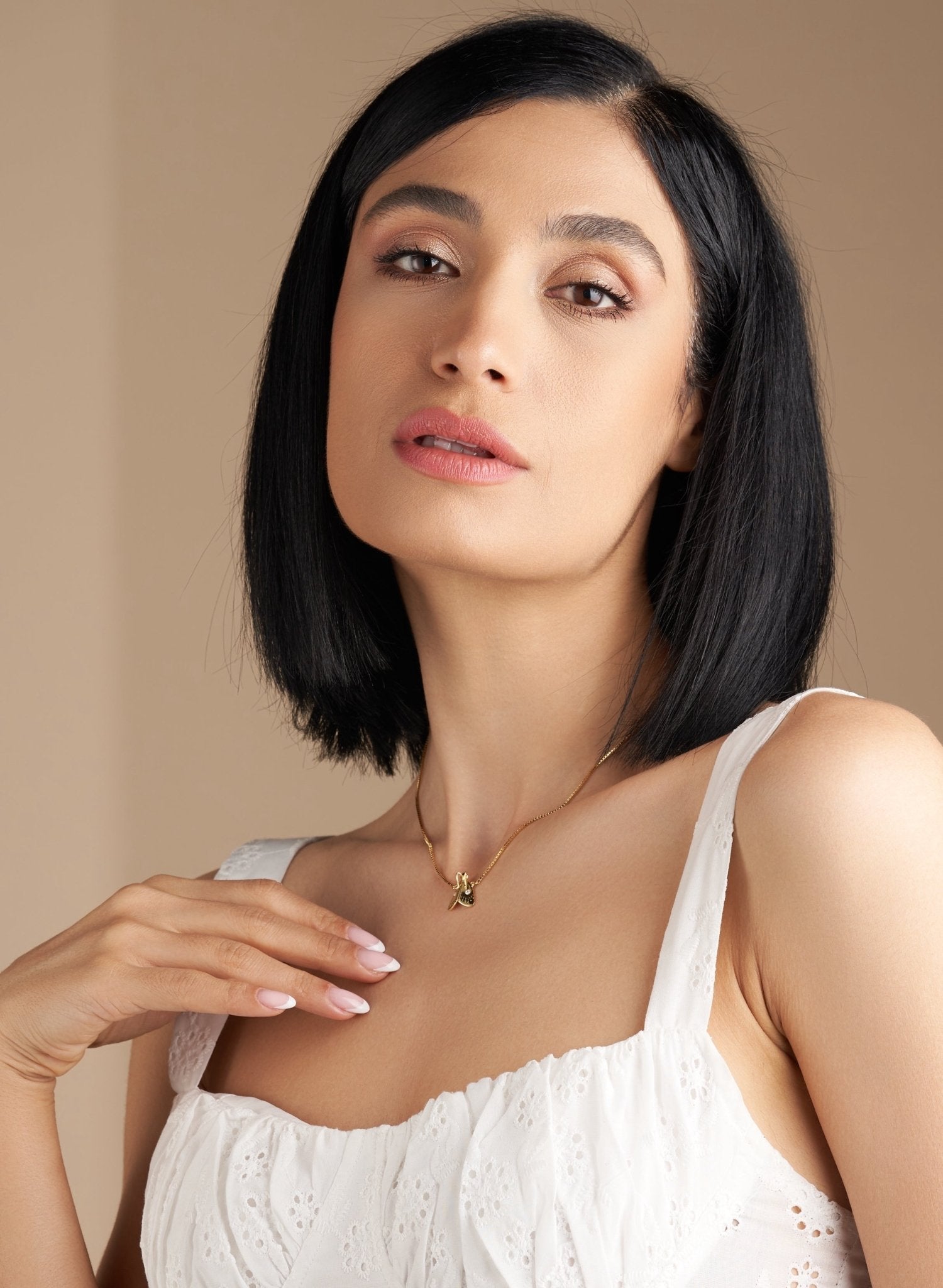 Model in white top with gold necklace, hand resting on chest