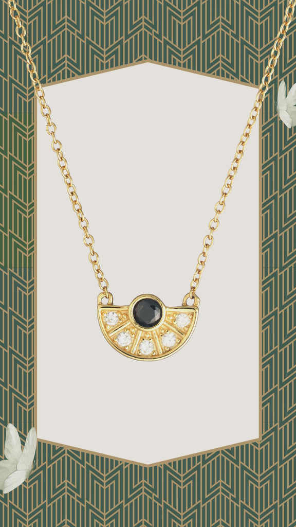 Gold necklace with black and white gemstone pendant on green pattern