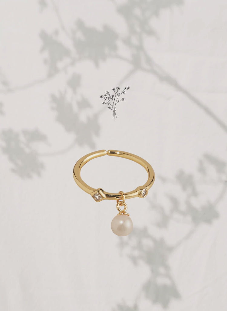 Gold ring with pearl charm and delicate shadowed floral background