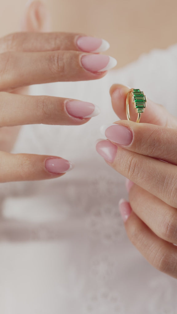 Hand holding a gold ring with green gemstones, close-up view